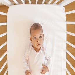 baby lying in a baby crib on a white fitted crib sheet