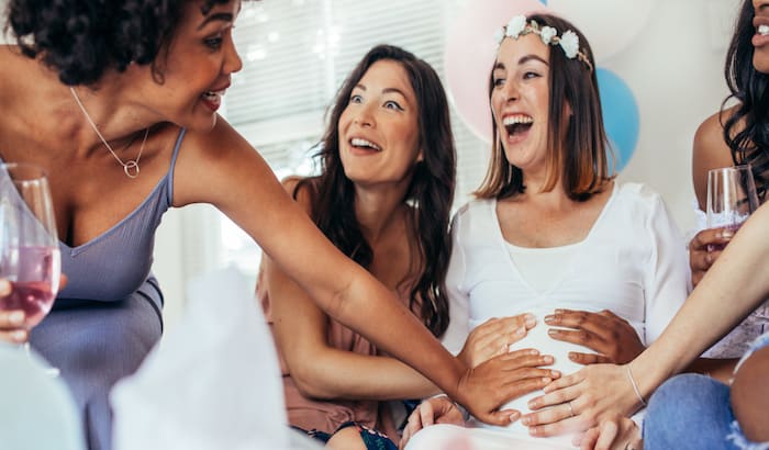 excited girlfriends touching a pregnant woman's belly at the baby shower