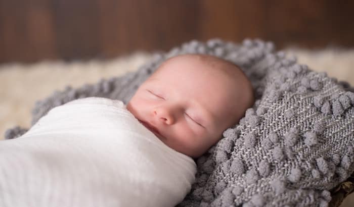 swaddled sleeping baby on a gray pillow